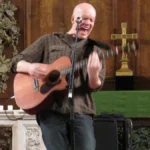 Devin Townsend performing solo with an acoustic guitar in a church